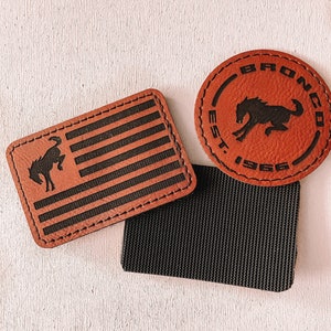 May include: Leather patches with a horse silhouette. One patch is rectangular with a flag design, and the other is circular with the text "BRONCO EST. 1966". A black fabric piece is also included.