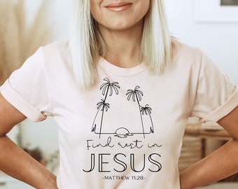 May include: A pink t-shirt with a black graphic design of palm trees and a sunset. The text "Find rest in JESUS -MATTHEW 11:28- " is printed on the shirt.