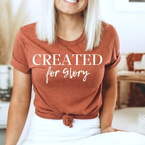 May include: A rust-colored t-shirt with the text "CREATED for glory" in white lettering.