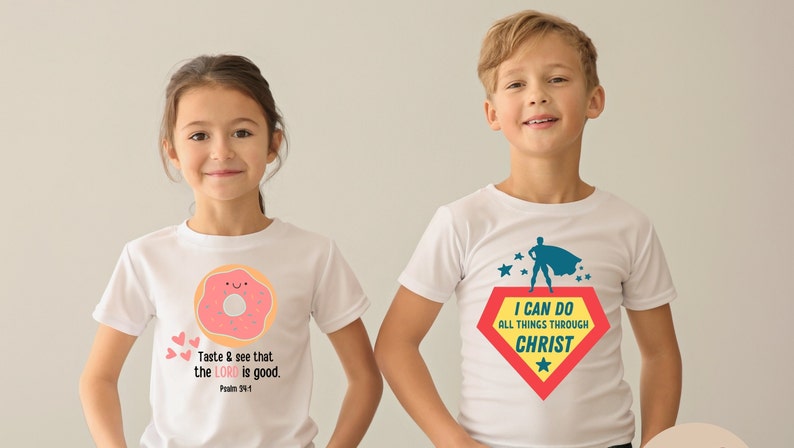 Puede incluir: Dos ni&ntilde;os con camisetas blancas con dise&ntilde;os diferentes. La camiseta de la ni&ntilde;a tiene un donut rosa con una cara sonriente y el texto "Taste & see that the LORD is good. Psalm 34:8". La camiseta del ni&ntilde;o tiene un superh&eacute;roe con una capa roja y amarilla y el texto "I CAN DO ALL THINGS THROUGH CHRIST".