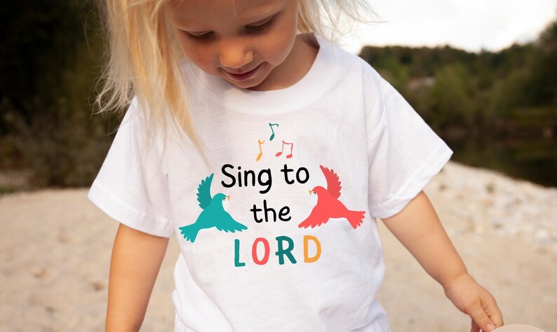 Puede incluir: Camiseta blanca con un dise&ntilde;o gr&aacute;fico colorido con dos p&aacute;jaros y el texto "Sing to the LORD".