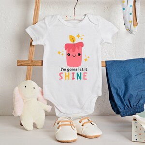 Puede incluir: Un body blanco para beb&eacute; con un gr&aacute;fico de vela roja y amarilla y el texto "I'm gonna let it SHINE".