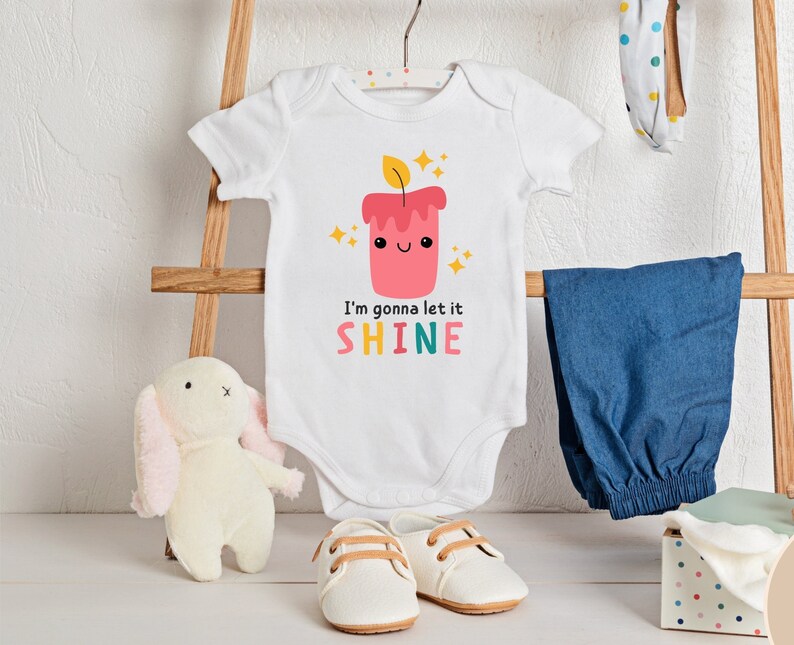 Puede incluir: Un body blanco para beb&eacute; con un gr&aacute;fico de vela roja y amarilla y el texto "I'm gonna let it SHINE".