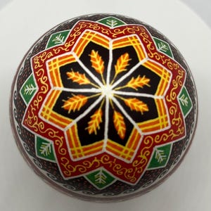 May include: A hand-painted Easter egg featuring a geometric design in shades of red, orange, yellow, green, and black.