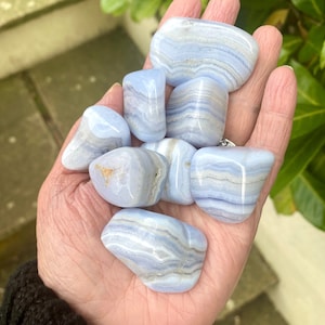 May include: A collection of blue lace agate tumbled stones. The stones are smooth and polished, with a variety of blue and white banding patterns.