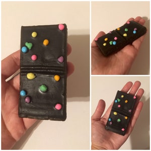 May include: A black domino with colorful, round, candy-like decorations. The domino is rectangular with a line dividing it into two sections. The candy dots are in various colors, including pink, yellow, blue, and orange.