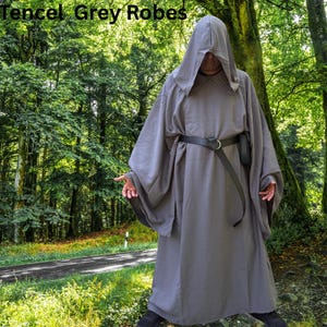 May include: A grey hooded robe with long, wide sleeves and a black belt featuring a metal ring buckle. The text Tencel Grey Robes is visible in the upper left corner. The garment is floor-length and features a loose, draped fit throughout.