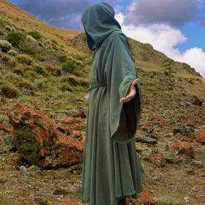 May include: A floor-length olive green hooded cloak featuring wide, flowing sleeves and a matching fabric belt secured with a silver-toned metal ring buckle. The garment is constructed with a deep hood and a full, pleated skirt that drapes downwards.