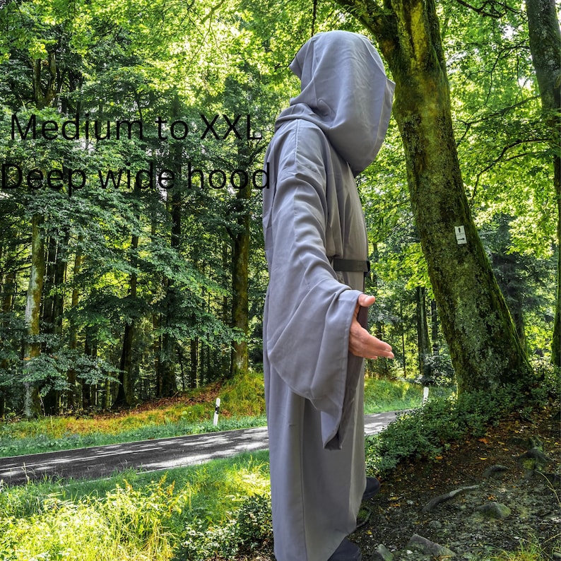 May include: A grey hooded robe with long, wide sleeves and a dark belt at the waist. The garment features a deep, wide hood and is available in sizes Medium to XXL. The robe is shown from the side, displaying its full-length, loose-fitting design.