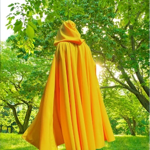 May include: A bright yellow hooded cloak featuring a full-length design with deep, vertical folds that drape from the shoulders to the hem. The garment includes a structured hood and a wide, flowing silhouette that extends outwards at the base.