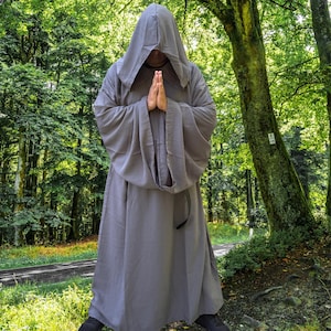 May include: A full-length, solid grey robe featuring long, wide sleeves and an attached hood that covers the head. The garment is constructed from a smooth, opaque fabric and hangs loosely from the shoulders to the floor, creating a draped silhouette.