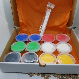 May include: A box containing 12 small tubs of colourful slime, each with a clear lid. The slime is in a variety of colours, including blue, green, red, white, black, and yellow. Two white plastic tools are included in the box.