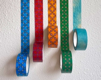 May include: Five rolls of patterned washi tape, each with a different design. The rolls are hanging from a white wall. The tape designs include blue and white, red and white, orange and white, green and white, and blue.