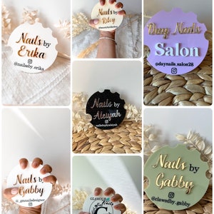 May include: A selection of car coasters, each branded for a nail salon. The coasters are in various colours, with gold or white lettering. Names such as "Erika," "Riley," "Aleyah," and "Gabby" are featured, along with Instagram handles.