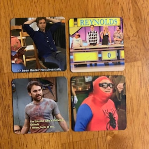 May include: Four square cards with images and text. The first card shows a man sitting in a chair with his arms behind his head. The text reads ">> been there? Not physically." The second card shows a game show set with four people standing behind a podium. The text reads "REYNOLDS" and "0". The third card shows a man wearing a red and blue shirt with a spider on it. The text reads "I'm the one who's thriving. Dennis. I mean, look at me." The fourth card shows a man wearing a red and blue superhero costume with a spider on it.