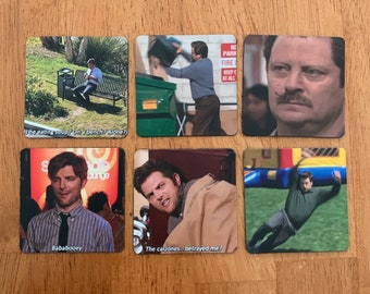 May include: Six square coasters with images of characters from the TV show "The Office". Each coaster has a different image and a caption. The captions are: "Is he eating soup? On a bench? Alone?", "Bababooey", "The calzones...betrayed me?", "No Parking Fire Keep Clear At All", and two other captions that are not visible in the image.