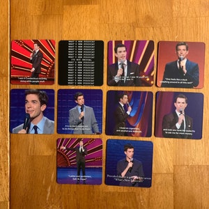 May include: A collection of square coasters featuring images of a comedian on stage. Each coaster has a different image and quote from the comedian's stand-up routine. The coasters are on a wooden surface.