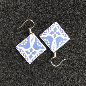 Puede incluir: Un par de pendientes de plata con abalorios cuadrados con estampado azul y blanco. Los abalorios tienen un diseño geométrico con puntos y líneas blancas.