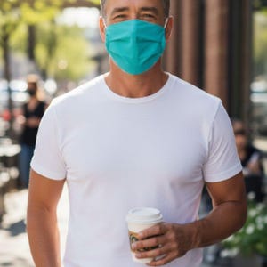 May include: A person wearing a teal face mask and a white t-shirt, holding a takeaway coffee cup. The person is outdoors on a sunny day. The background includes a brick building and foliage.