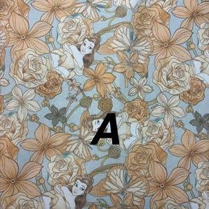 Pu&ograve; includere: Tessuto fantasia con un personaggio dei cartoni animati, fiori e farfalle nei toni del beige, crema e azzurro. La lettera "A" &egrave; stampata in nero sul tessuto.