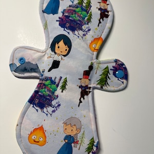 May include: A white cloth pad with a colorful print of characters and a flying house from the animated film "Howl's Moving Castle".