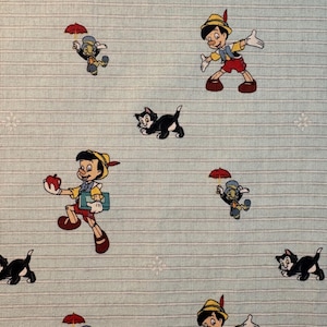 May include: Light blue fabric with a repeating pattern of Pinocchio, Jiminy Cricket, and black cats. Pinocchio is depicted in his classic outfit, and Jiminy Cricket holds a red umbrella. The background has white stripes and snowflake accents.