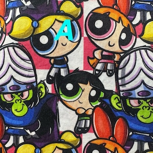 Può includere: Un tessuto colorato con un motivo ripetitivo di personaggi dei cartoni animati. I personaggi includono un mostro verde, una ragazza rosa con le trecce e una ragazza blu con le trecce. Il tessuto ha uno sfondo a scacchi.