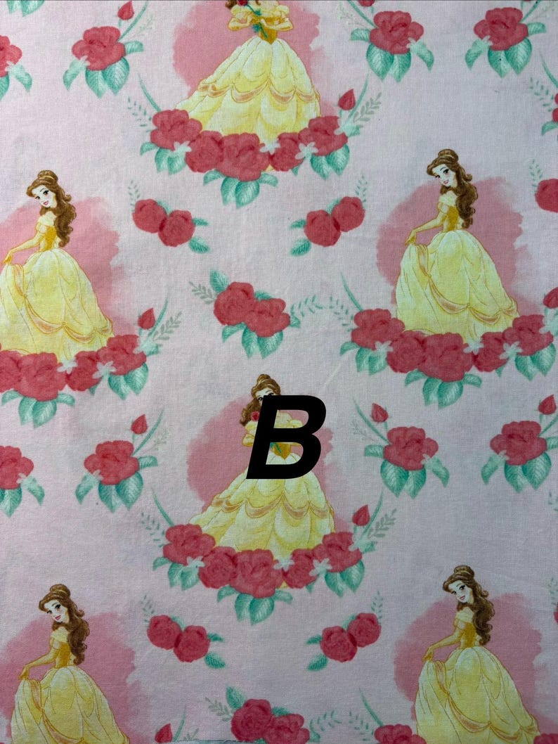 Pu&ograve; includere: Tessuto rosa con un motivo ripetuto di una principessa in abito giallo, circondata da rose rosse e foglie verdi. La principessa ha i capelli castani ed &egrave; ambientata su uno sfondo rosa con un disegno circolare rosa pi&ugrave; chiaro.