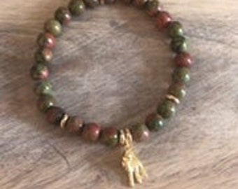 May include: A green, brown, and red unakite beaded bracelet with a gold-colored charm in the shape of a hand. The charm is labeled "Guyan Mudra".