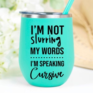 May include: A turquoise stainless steel tumbler with a black inscription that reads "I'm not slurring my words I'm speaking cursive".
