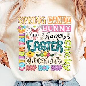 May include: A white t-shirt with a colorful graphic design featuring the text "Spring Candy Bunny Happy Easter Chickly Chocolate Hop Hop Hop".