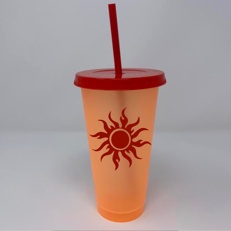 May include: A clear orange tumbler with a red lid and a red straw. The tumbler has a red sun with flames design on the front.