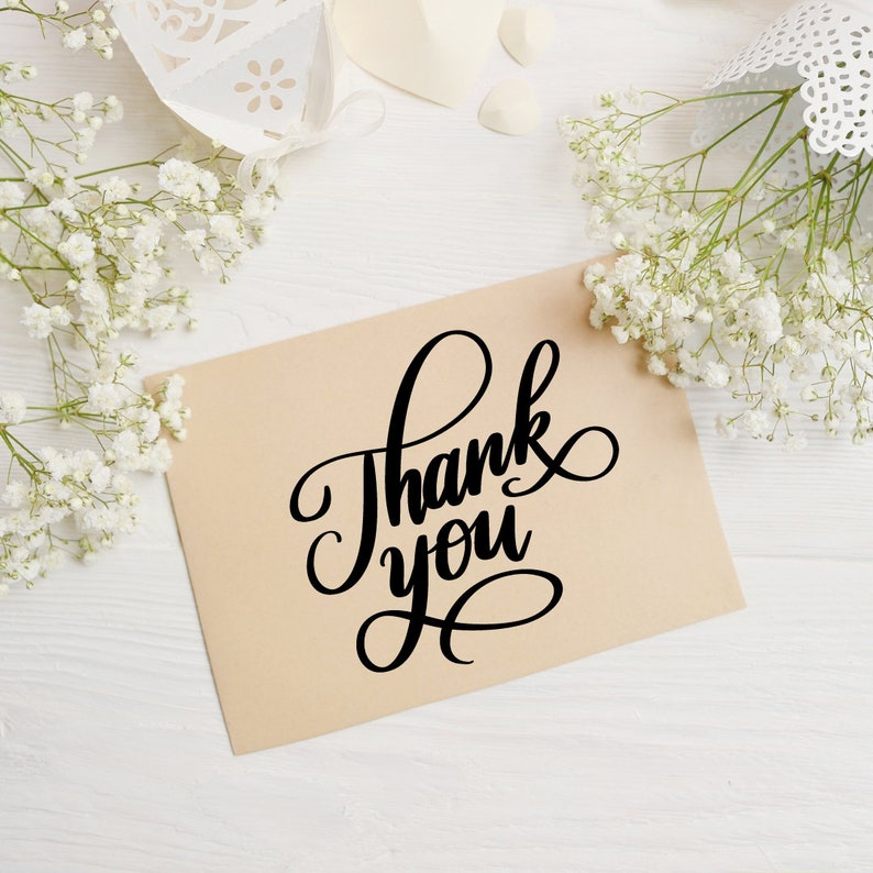May include: A brown card with the text "Thank you" written in black cursive script. The card is surrounded by white baby's breath flowers.