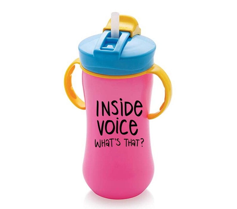 May include: Pink plastic sippy cup with yellow handles and a blue lid. The cup has a straw and says "Inside Voice What's That?" on the front.