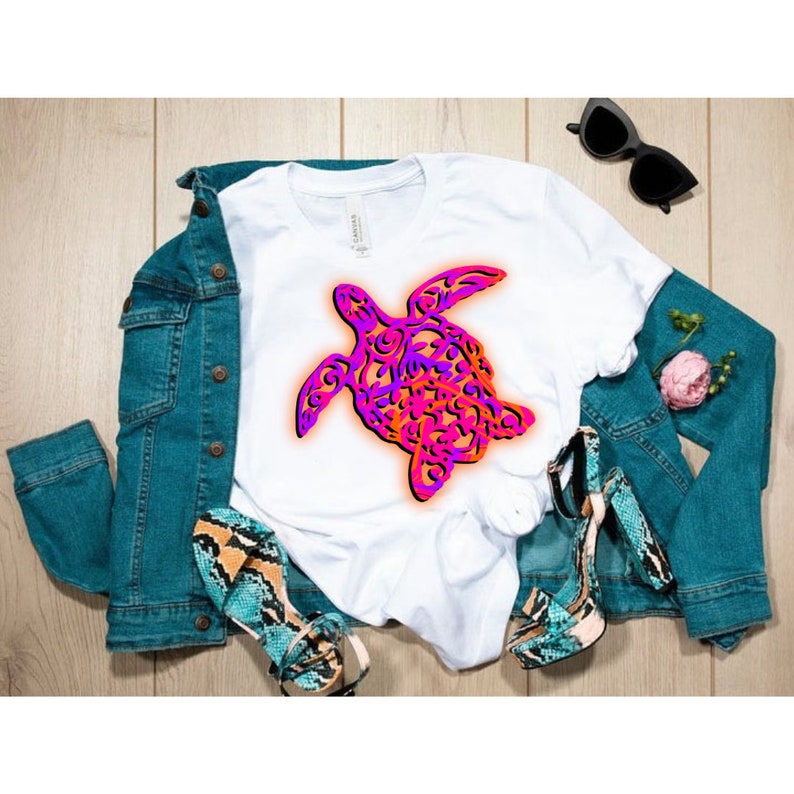 K&ouml;nnte beinhalten: Ein wei&szlig;es T-Shirt mit einer pinkfarbenen und orangen Grafik einer stilisierten Meeresschildkr&ouml;te. Die Schildkr&ouml;te ist schwarz umrandet und hat ein detailliertes Design.