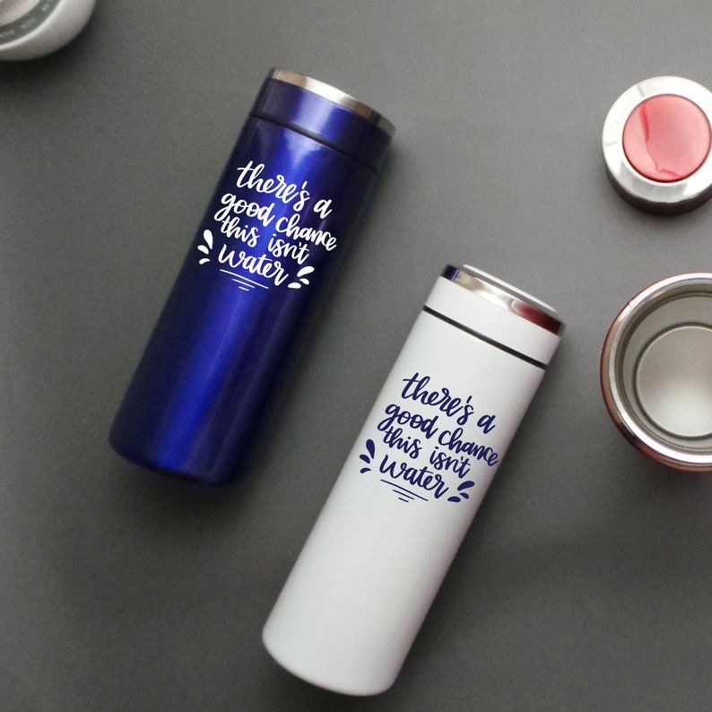 May include: Two stainless steel travel mugs with a white inscription that reads "there's a good chance this isn't water". One mug is blue and the other is white.