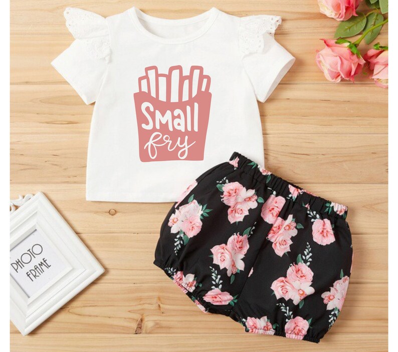 May include: A white short-sleeved t-shirt with a pink graphic of french fries and the text "Small fry". The shirt is paired with black shorts with a pink floral print.