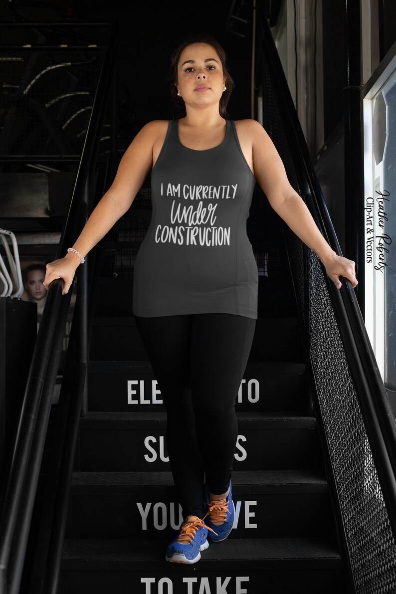 K&ouml;nnte beinhalten: Ein dunkelgraues Tanktop mit dem wei&szlig;en Schriftzug "I AM CURRENTLY UNDER CONSTRUCTION". Die Person tr&auml;gt schwarze Leggings und blaue und orangefarbene Turnschuhe. Das Bild ist auf einer schwarzen Treppe aufgenommen.