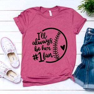 May include: A pink t-shirt with a black baseball graphic and the text "I'll always be her #1 fan".