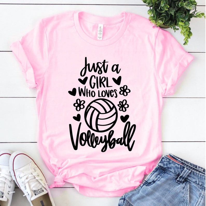 May include: Pink t-shirt with a black graphic that says "Just a girl who loves volleyball" with a volleyball graphic and hearts and flowers.