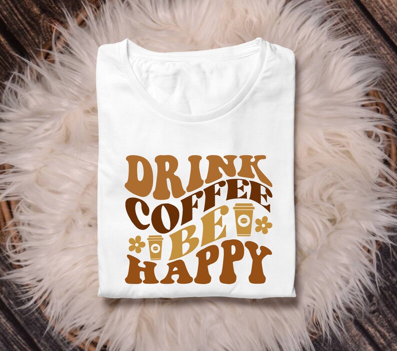 May include: White t-shirt with brown text that reads "Drink Coffee Be Happy" in a retro font. The text is surrounded by brown coffee cup illustrations.