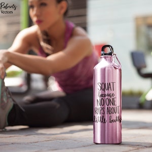 K&ouml;nnte beinhalten: Eine rosafarbene Edelstahl-Trinkflasche mit schwarzem Deckel und Karabinerhaken. Auf der Flasche steht in schwarzer Schrift "SQUAT because NO ONE RAPS ABOUT little butts". Die Flasche steht auf einer Betonoberfl&auml;che.