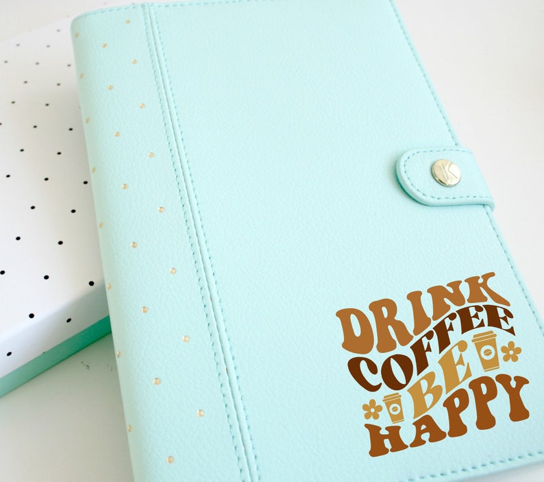 May include: A light blue leather planner with gold polka dots and a brown vinyl sticker that says "Drink Coffee Be Happy" with coffee cup illustrations.