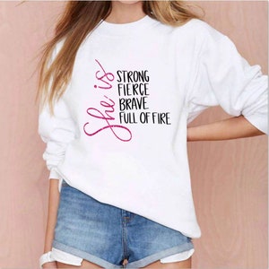 May include: White sweatshirt with pink glitter lettering that reads "She is strong fierce brave full of fire".