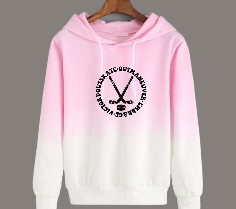May include: Pink and white ombre hoodie with a black circle graphic featuring hockey sticks and the text "Outmaneuver. Outskate.  Embrace. Victory."