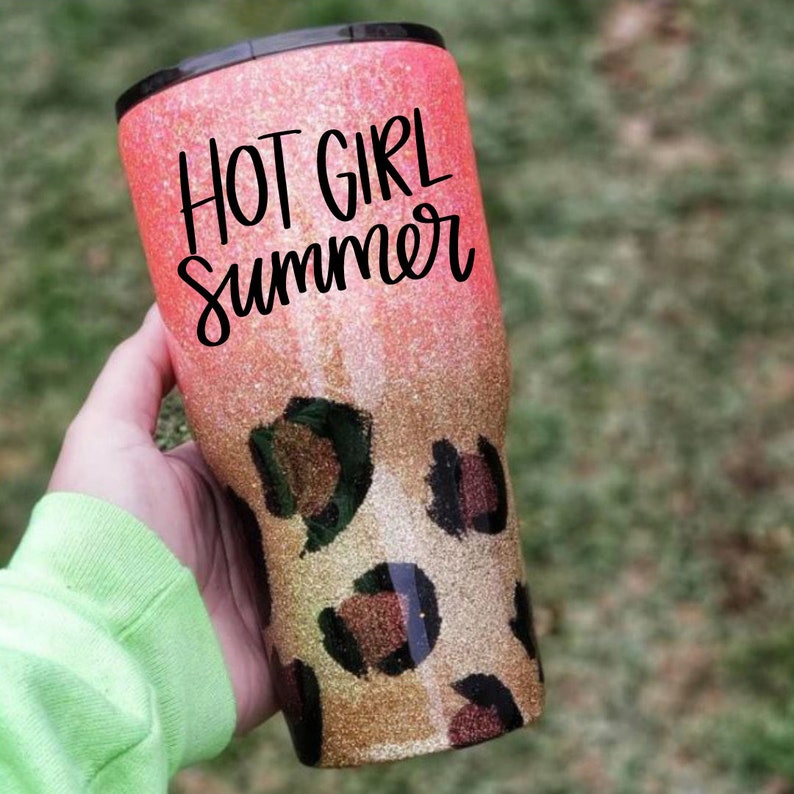 May include: A pink and gold glitter tumbler with a leopard print design. The tumbler has black lettering that says "Hot Girl Summer".