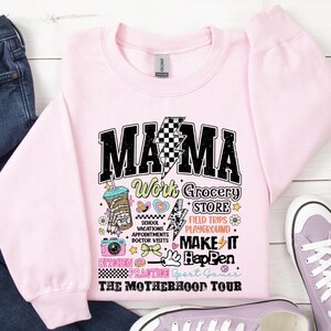 May include: Pink sweatshirt with a black and white graphic that says "Mama Work Grocery Store Field Trips Playground Make It Happen The Motherhood Tour".