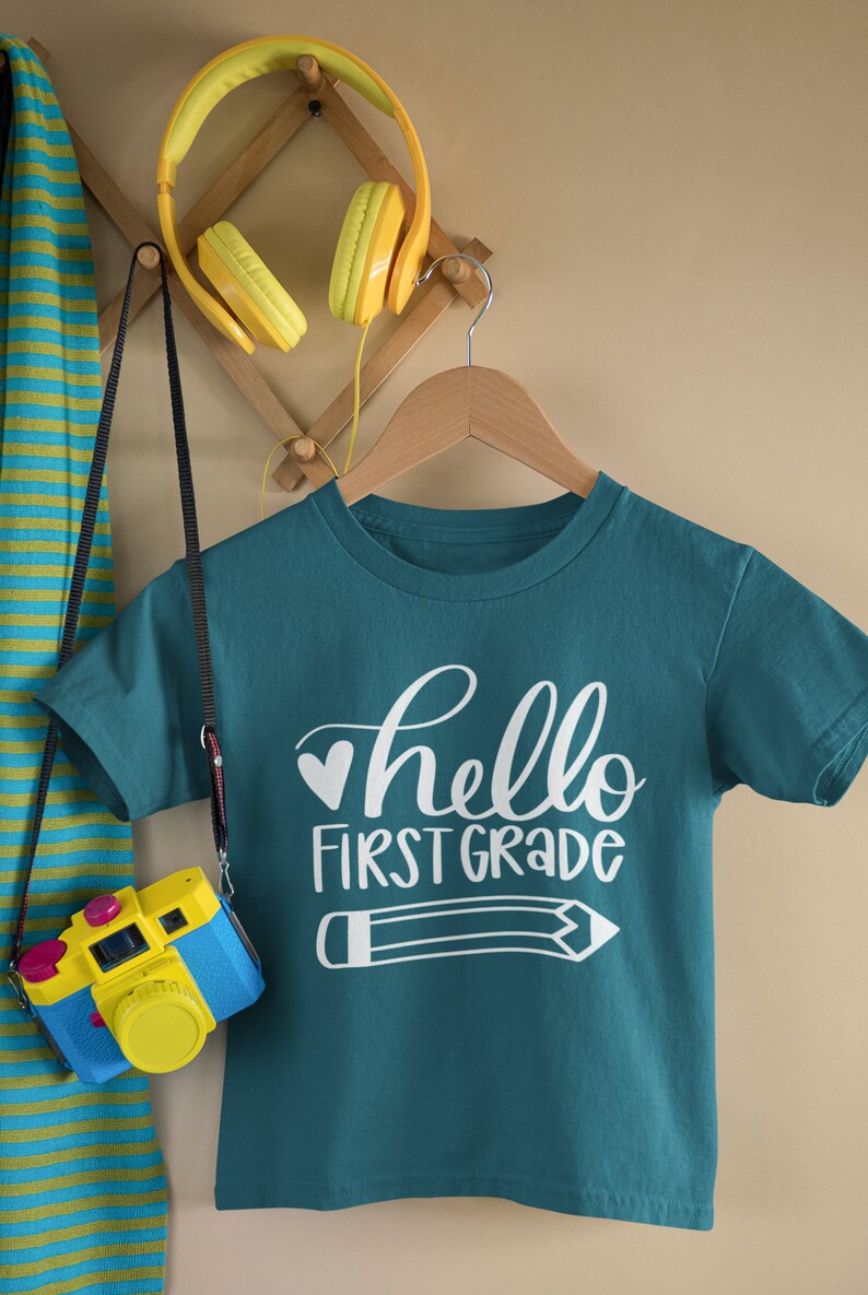 May include: Teal blue t-shirt with white text that says "hello first grade" and a white pencil graphic.