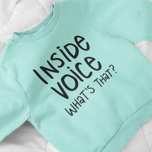 May include: A light blue sweatshirt with black text that reads "Inside Voice What's That?"