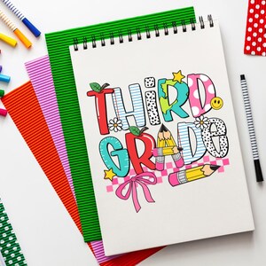 Puede incluir: Una libreta blanca con espiral y un dise&ntilde;o colorido que dice "Tercer Grado". La libreta est&aacute; rodeada de l&aacute;pices de colores y otros &uacute;tiles escolares.
